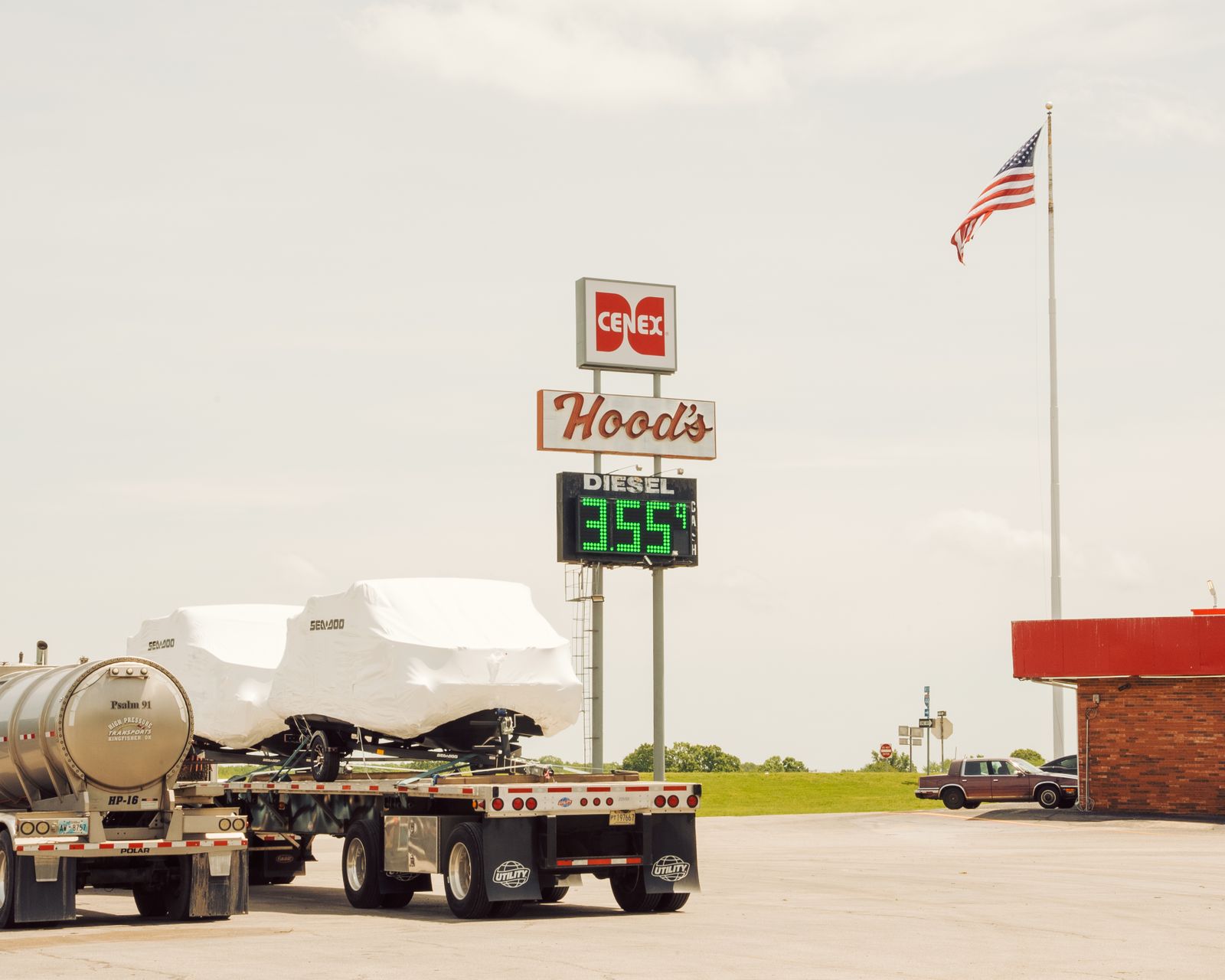 A freight truck refueling with diesel at a gas station, with the high price visible on the pump.