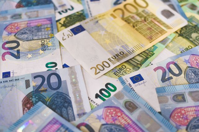 Manos sosteniendo billetes de dólar y pesos mexicanos con gráficos financieros de fondo.