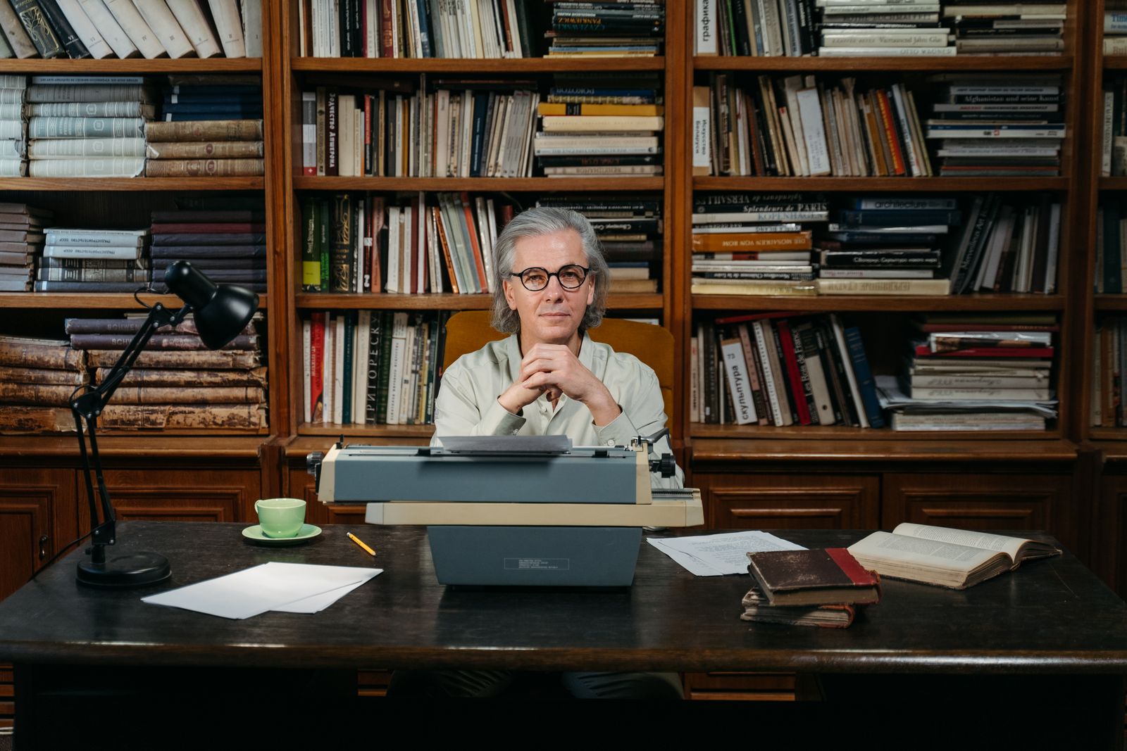 Miguel Brascó, un hombre mayor de aspecto distinguido, sentado en un estudio rodeado de libros, con una expresión pensativa y cálida.