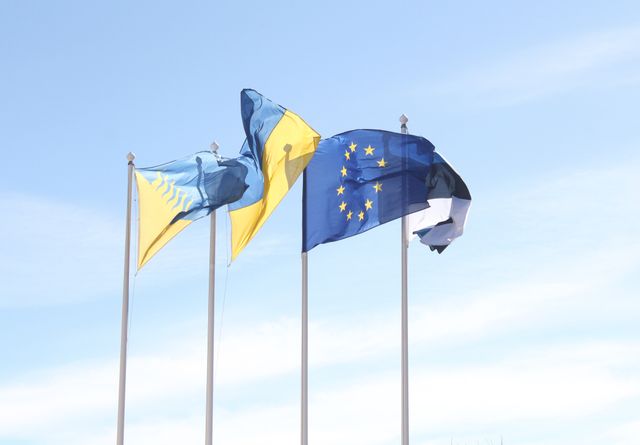 Banderas de Canadá y la Unión Europea ondeando juntas frente a un edificio gubernamental moderno.