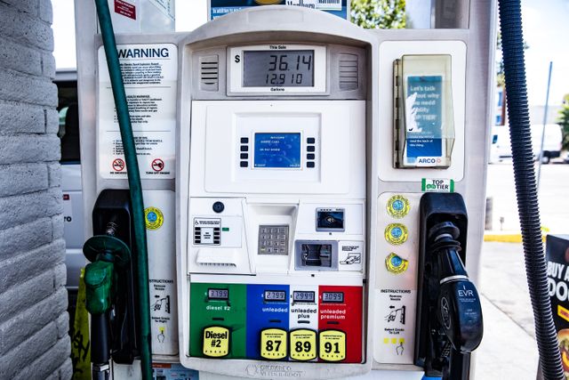 Mano sosteniendo una bomba de gasolina con un precio elevado en la pantalla digital.