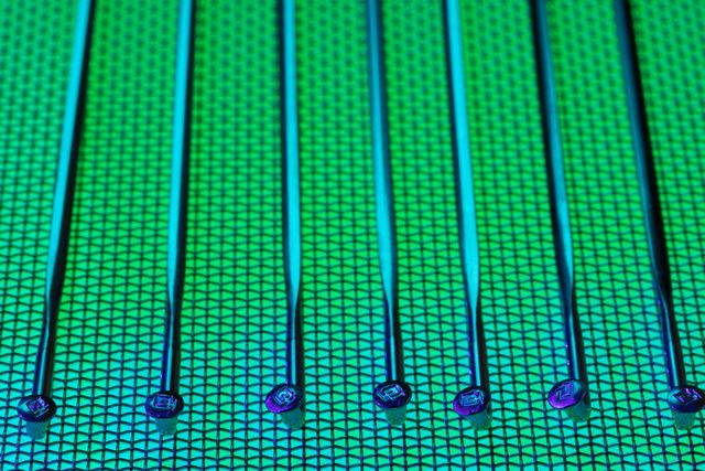 A silicon wafer with intricate circuits, held by a gloved hand, with a blurred data center in the background.